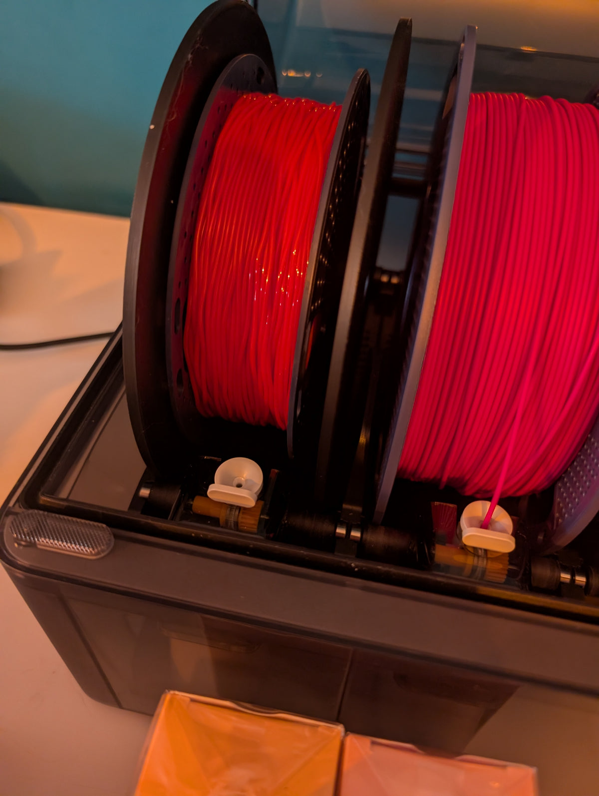 Two red filament spools fitted with black reusable spool adapters inside a 3D printer