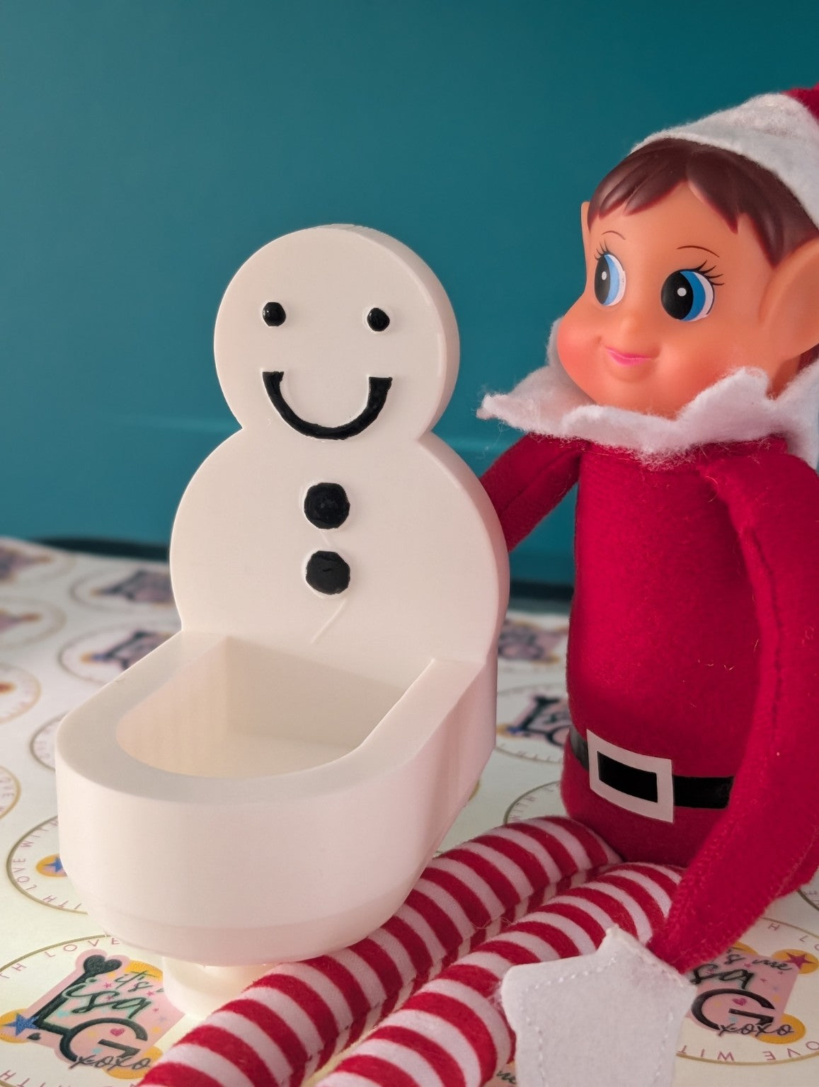 White 3D printed Elf Toilet with snowman back shown beside a Christmas elf